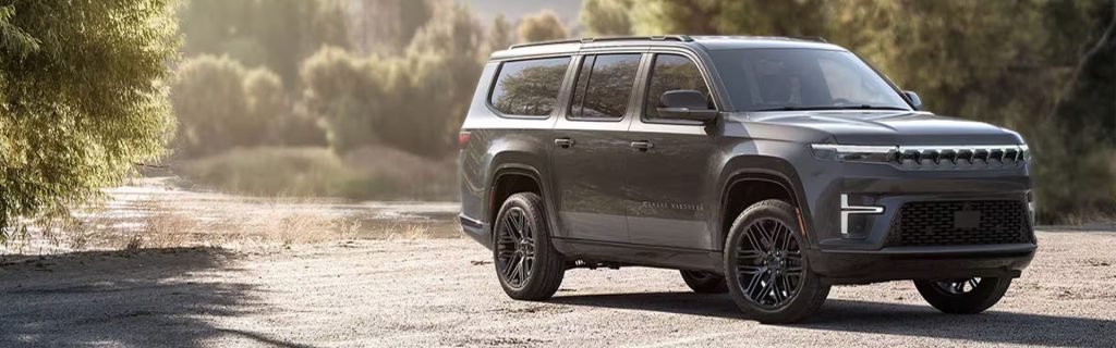 A dark gray SUV parked on a dirt road surrounded by trees.
