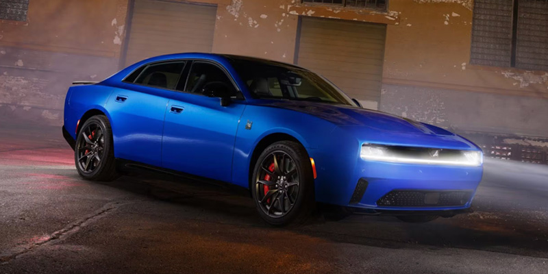 Bright blue Dodge Charger EV sedan parked in an industrial alleyway at night.
