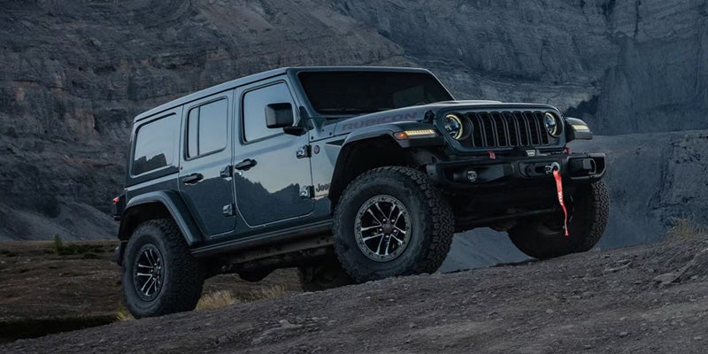 A 2026 Jeep Wrangler climbing a dirt mountain road at night